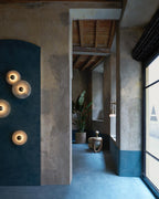 Four Clérachic lit sconces mounted on a teal-painted arch in a plastered hallway, seen from across the room.