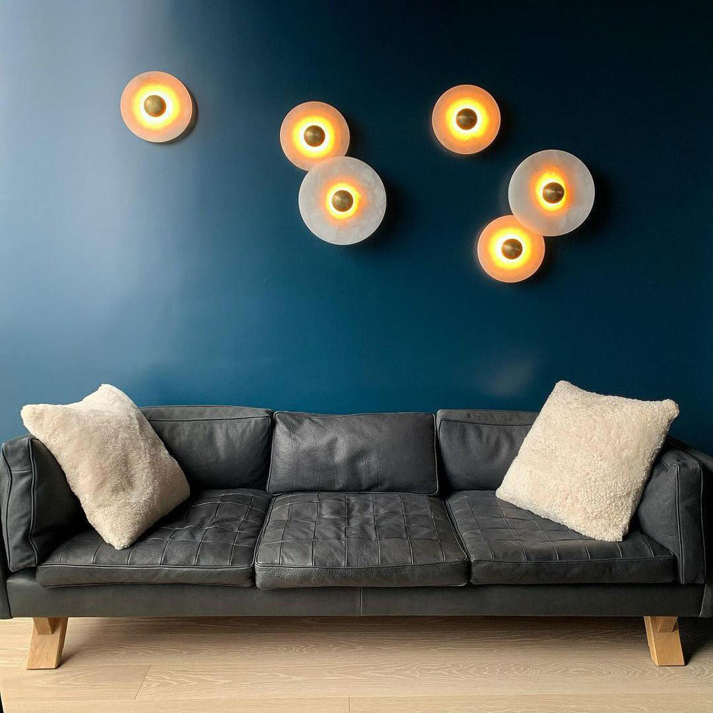 Clérachic six lit sconces clustered on a deep blue wall above a grey leather sofa, glowing warm amber.