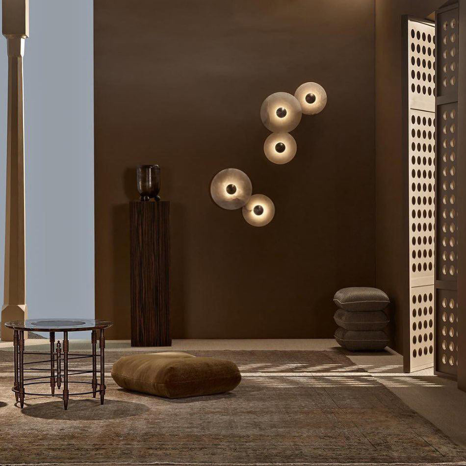 Clérachic five sconces overlapping in a diagonal cluster on a chocolate-brown wall beside a low seating area.