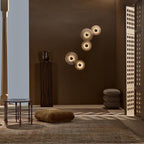 Clérachic five sconces overlapping in a diagonal cluster on a chocolate-brown wall beside a low seating area.