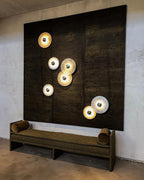 Clérachic seven sconces scattered across a dark bronze panel above an olive daybed, each disc lit behind its boss.
