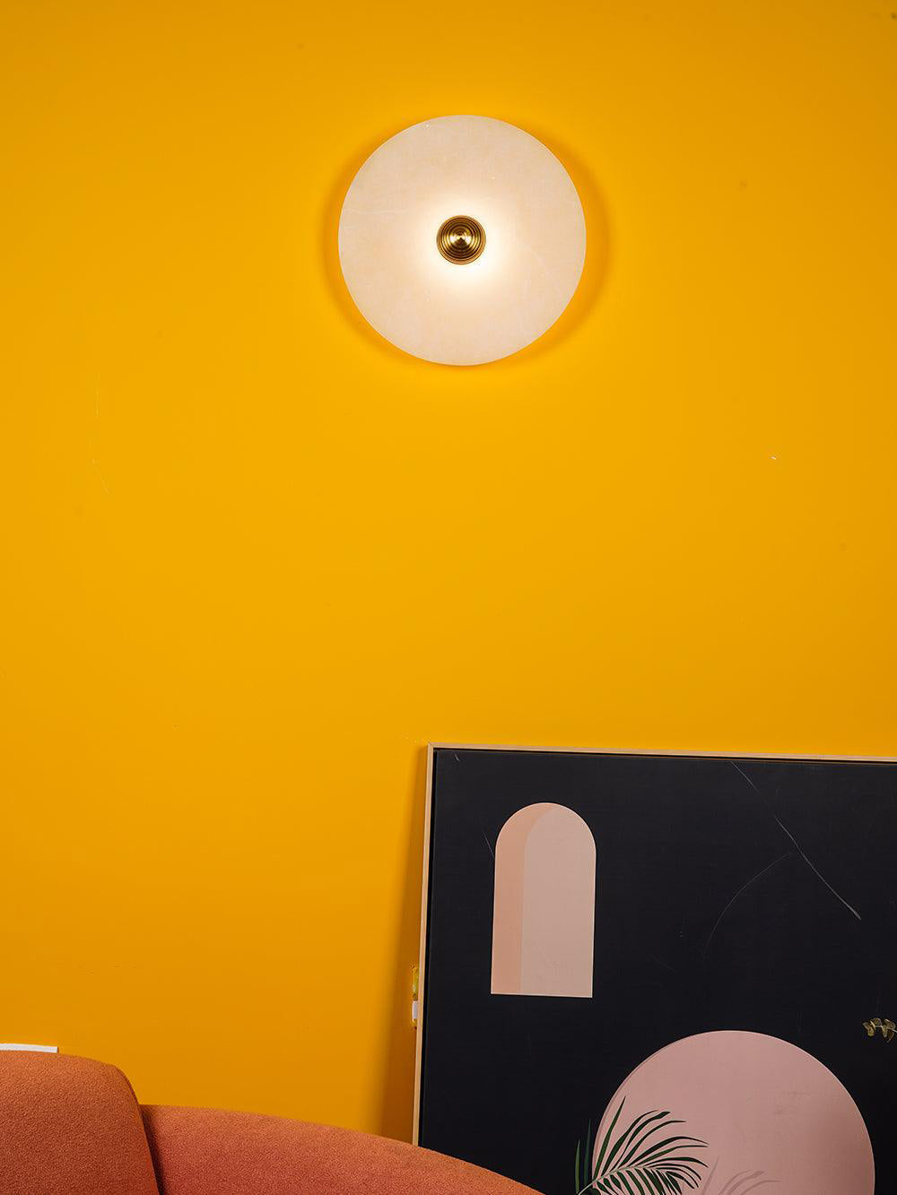 Clérachic one lit sconce on a bright yellow wall above a leaning graphic print and a rust-coloured sofa.