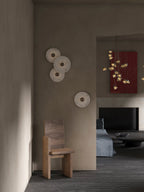 A Clérachic cluster of three sconces plus a single lower disc on a taupe plaster wall above a wooden chair.