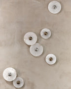 Clérachic seven unlit sconces arranged across a beige plaster wall, showing both brass and steel centre bosses.