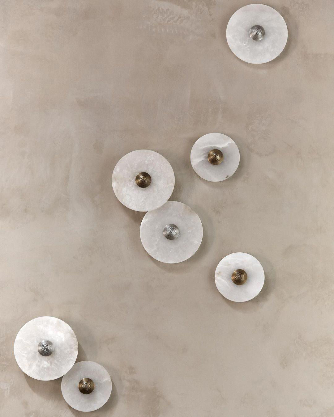 Clérachic seven unlit sconces arranged across a beige plaster wall, showing both brass and steel centre bosses.