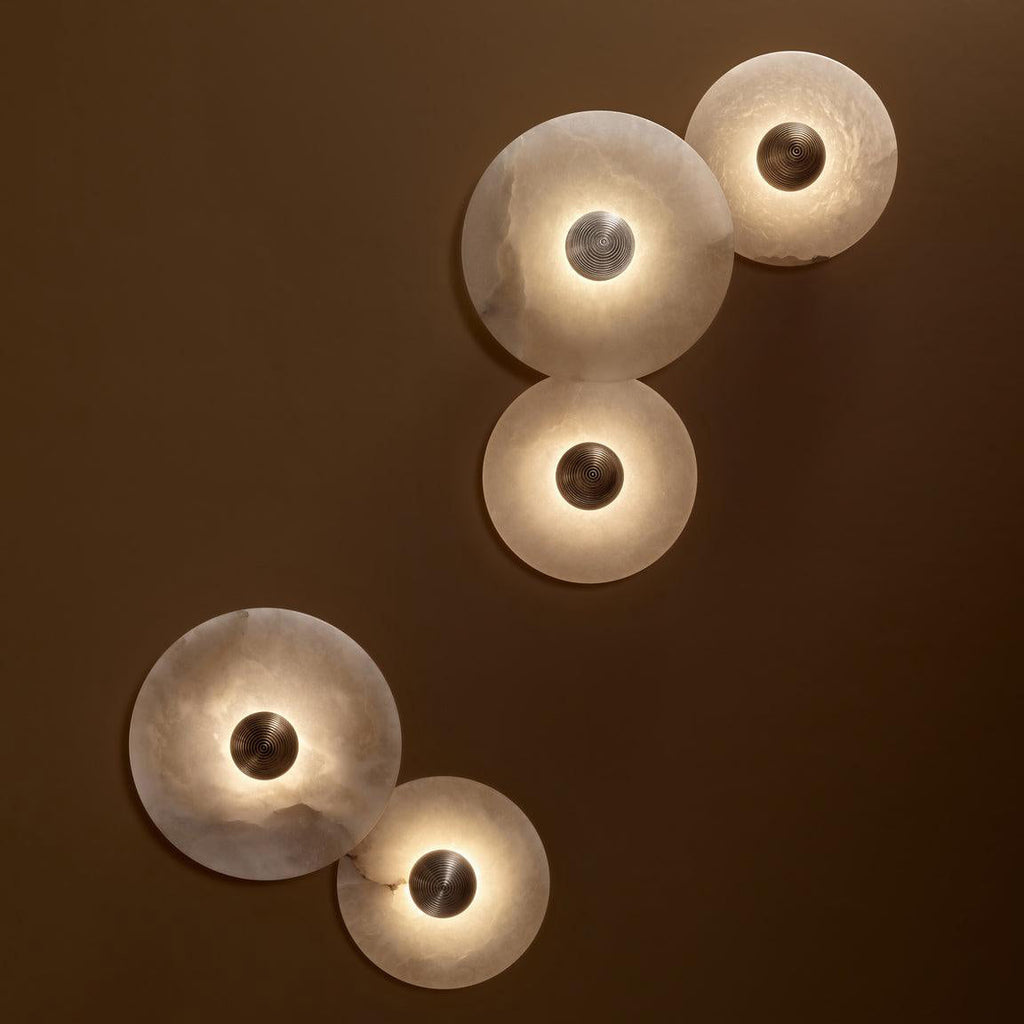 Clérachic five lit sconces in two diagonal clusters on a brown wall, backlight washing around each stone disc.