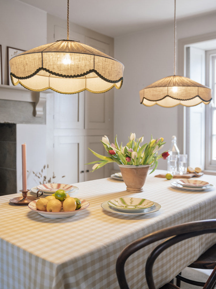 A long gingham-covered table is set beneath two of this Clérachic pendant, with tulips and citrus fruit.