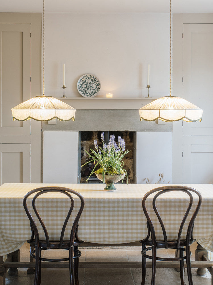 Two of this Clérachic pendant hang above a gingham-clothed table set with bentwood chairs, near a stone fireplace.