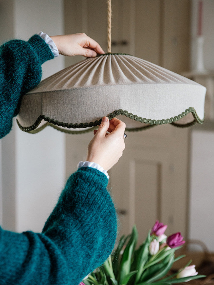 A hand adjusts the scalloped green trim on this Clérachic pendant's shade, with tulips visible below.