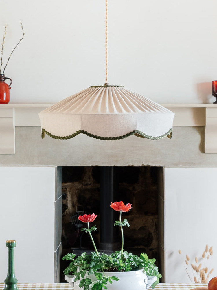 This Clérachic pendant hangs above a stone mantelpiece, near red flowers in a small white pot.