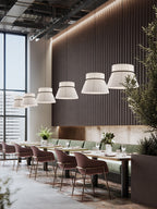 Five pleated beige Clérachic pendants glow in a row above a restaurant banquette lined with velvet chairs.