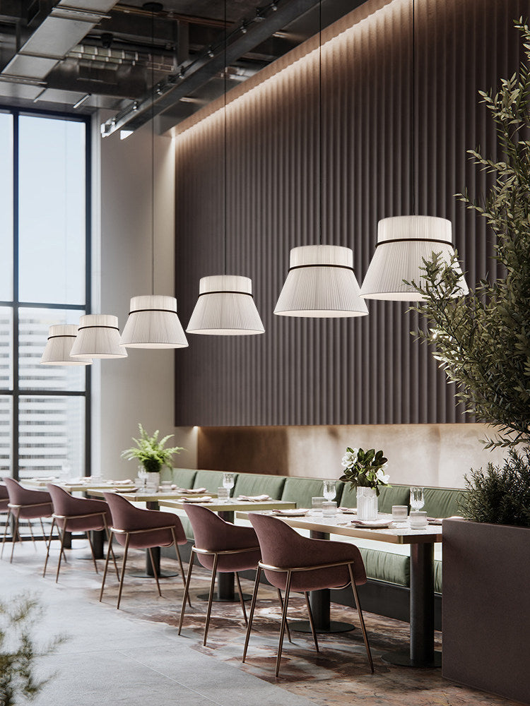 Five pleated beige Clérachic pendants glow in a row above a restaurant banquette lined with velvet chairs.