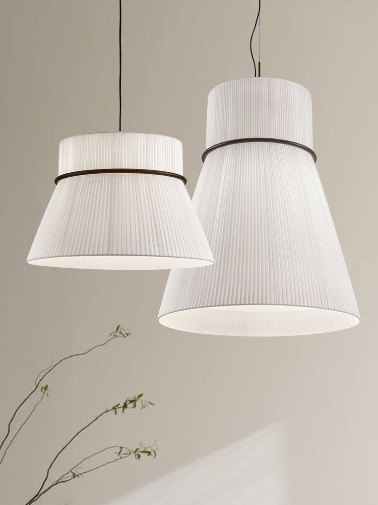Two pleated Clérachic pendants hang together against a plain grey backdrop, styled beside a few bare branches.