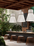 Three pleated Clérachic pendants light an outdoor bar counter lined with woven stools and potted greenery.