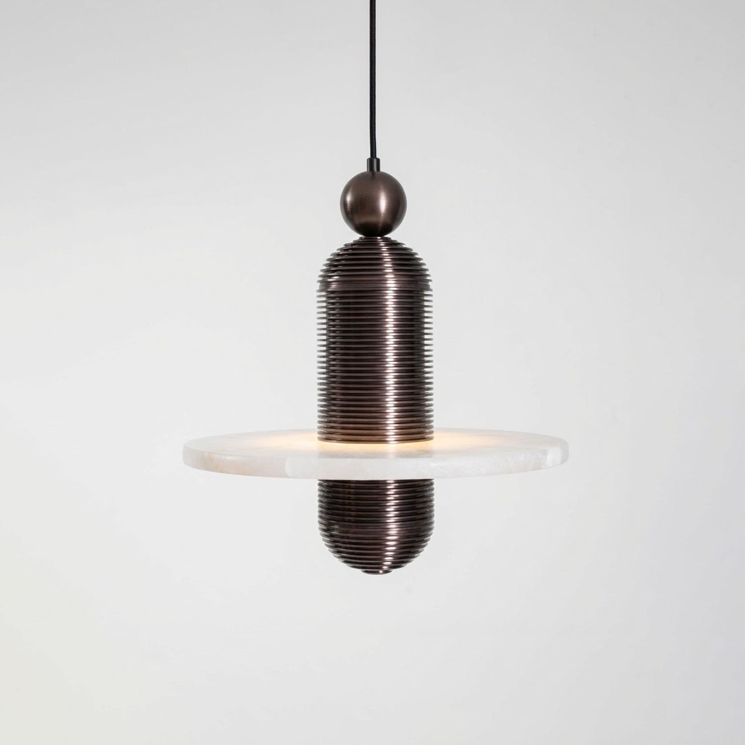 Saturn alabaster pendant light in dark bronze, single stone disc lit from within, side view on grey
