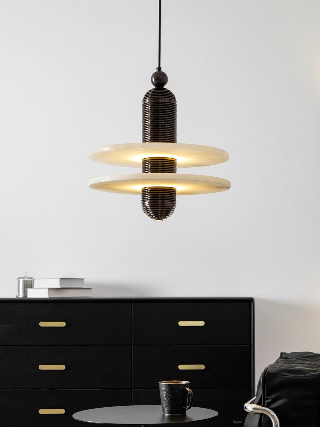 Dark bronze Saturn pendant lit above a long black sideboard, showing the drop from ceiling to disc