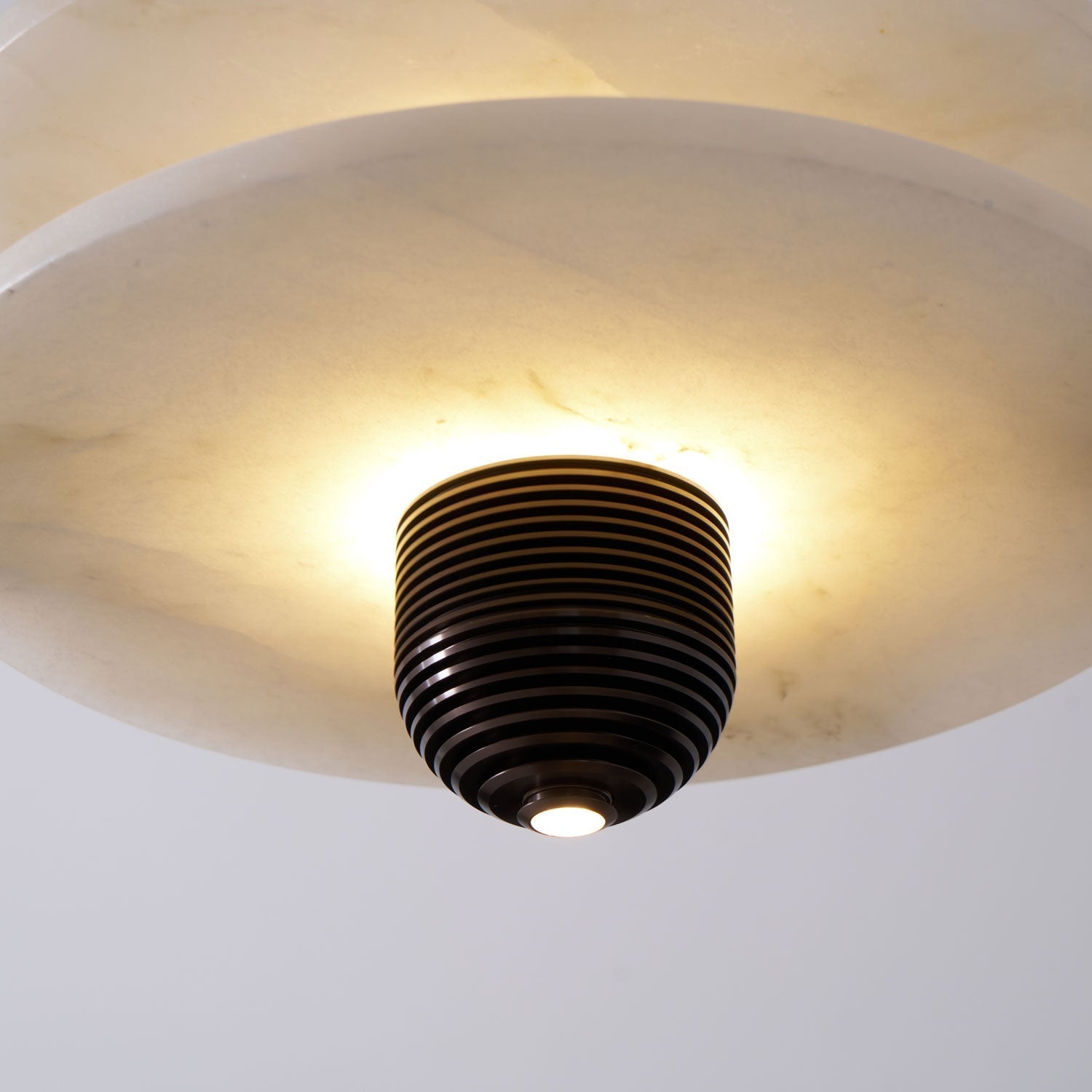 Underside view of the alabaster disc and ribbed bronze finial with the light source glowing