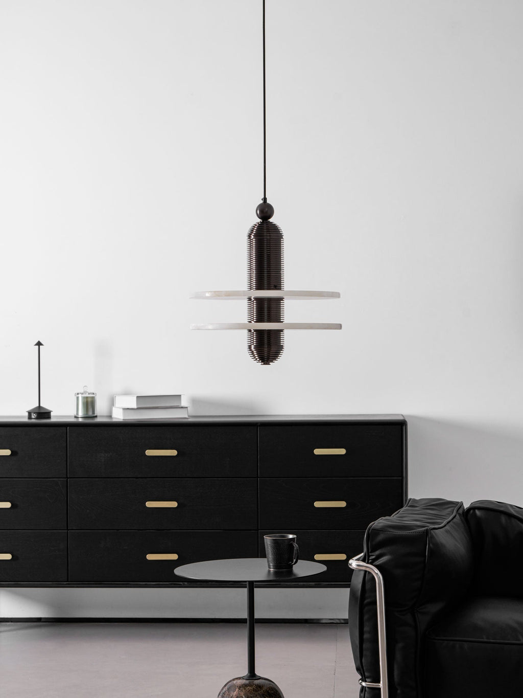 Wide interior view with the dark bronze Saturn pendant above a black sideboard and low side table
