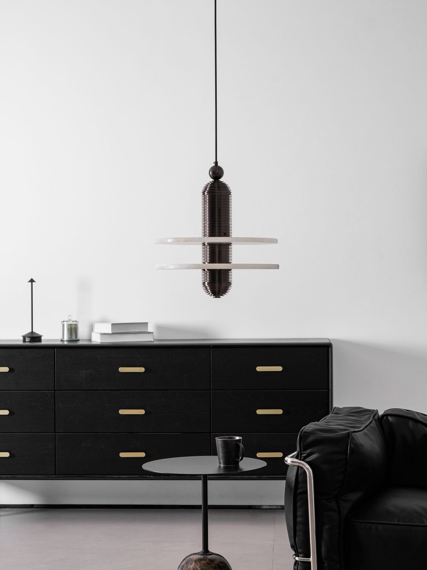 Wide interior view with the dark bronze Saturn pendant above a black sideboard and low side table