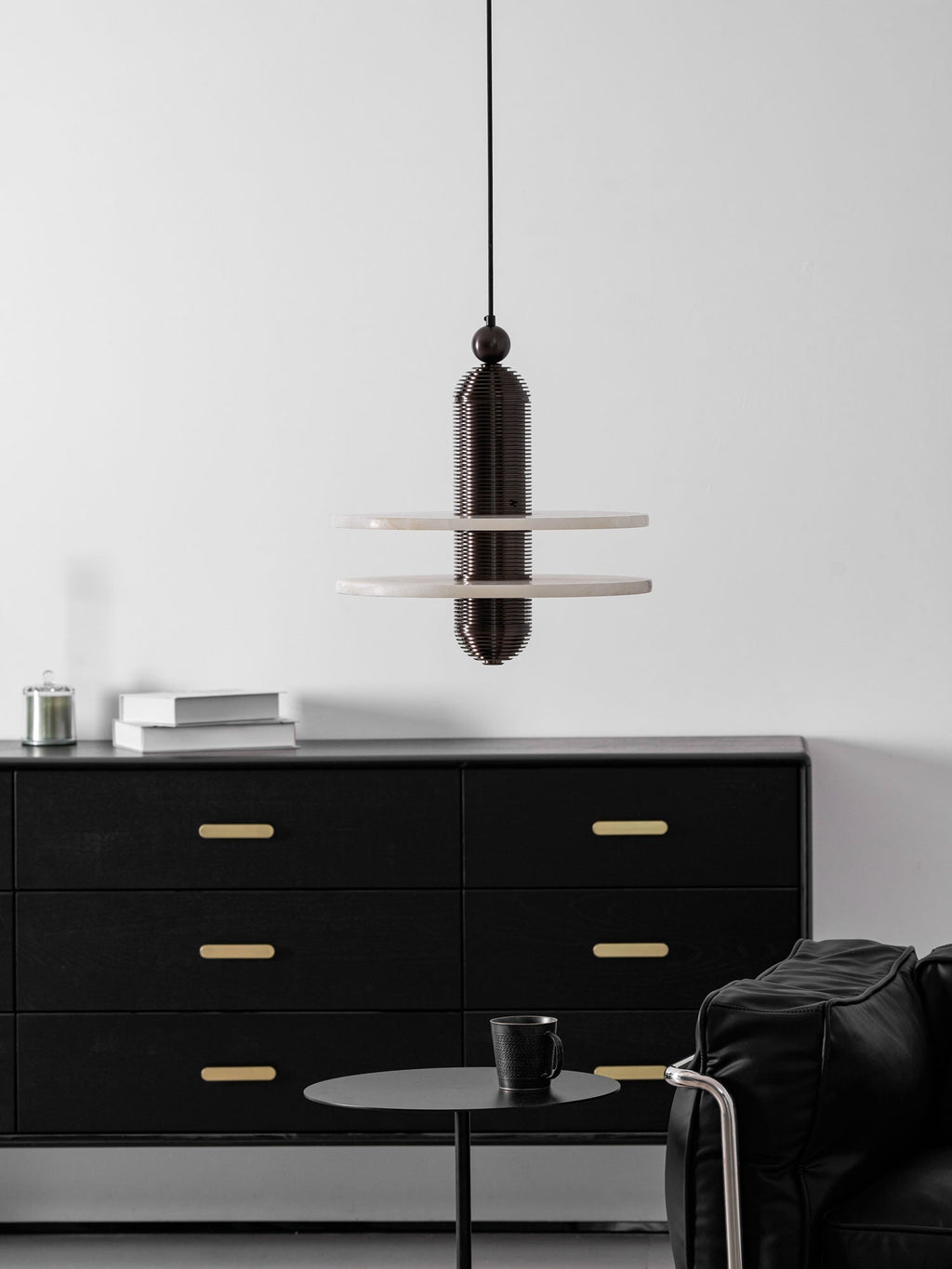 Dark bronze Saturn pendant with two alabaster discs above a black oak sideboard, seen from a distance