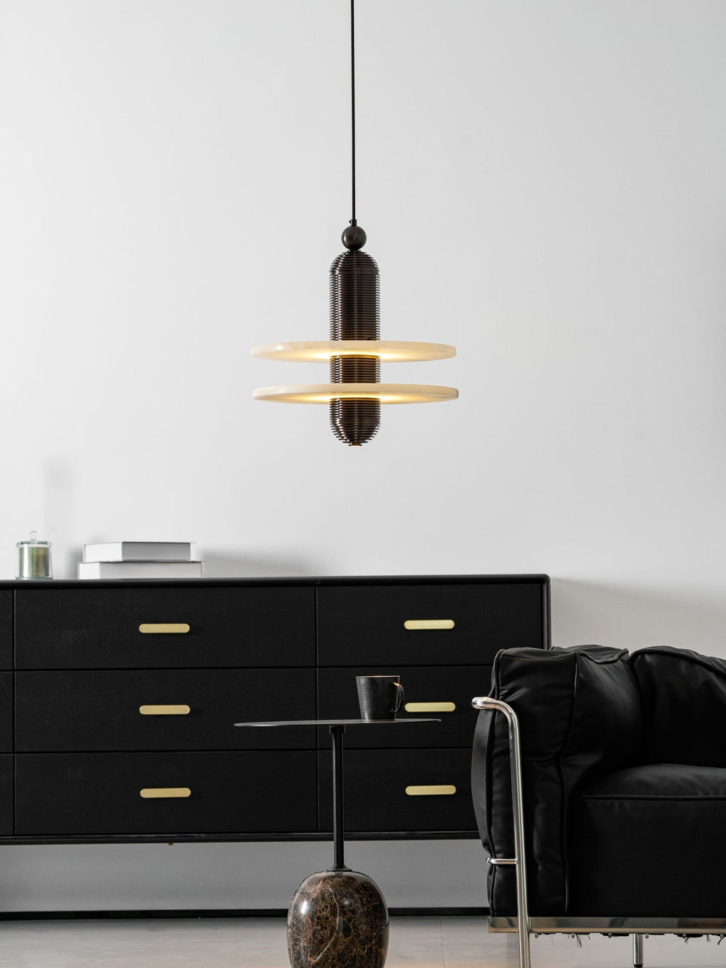 Saturn pendant in dark bronze lit above a black sideboard, glow caught under both stone discs