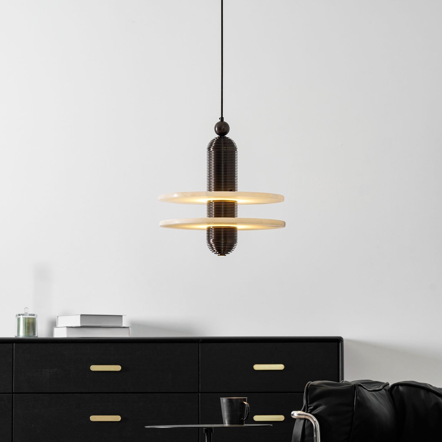 Dark bronze Saturn pendant centred on a white wall, light spilling from between the two discs