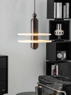 Dark bronze Saturn pendant beside black shelving and art books, both discs lit from the inside