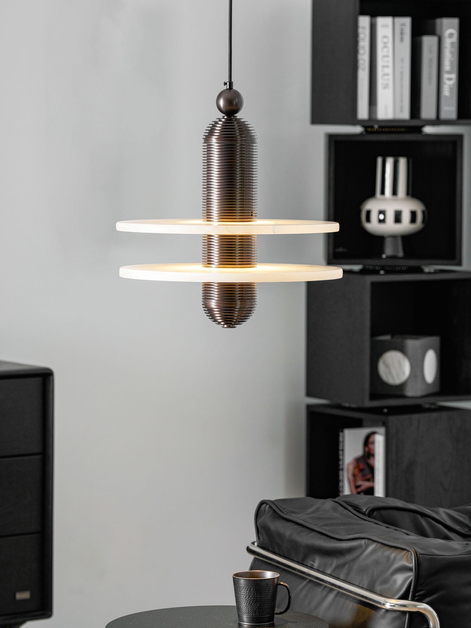 Dark bronze Saturn pendant beside black shelving and art books, both discs lit from the inside