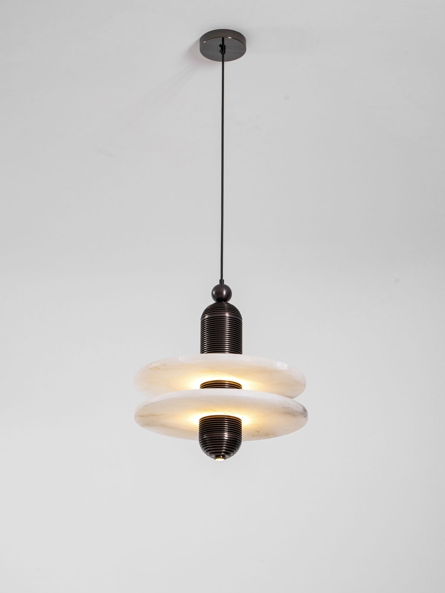 Full length of the lit Saturn pendant, both alabaster discs glowing beneath the ceiling canopy
