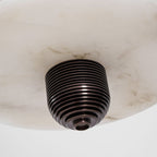 Macro of the ribbed bronze finial under the alabaster disc, showing the stone's grey veining