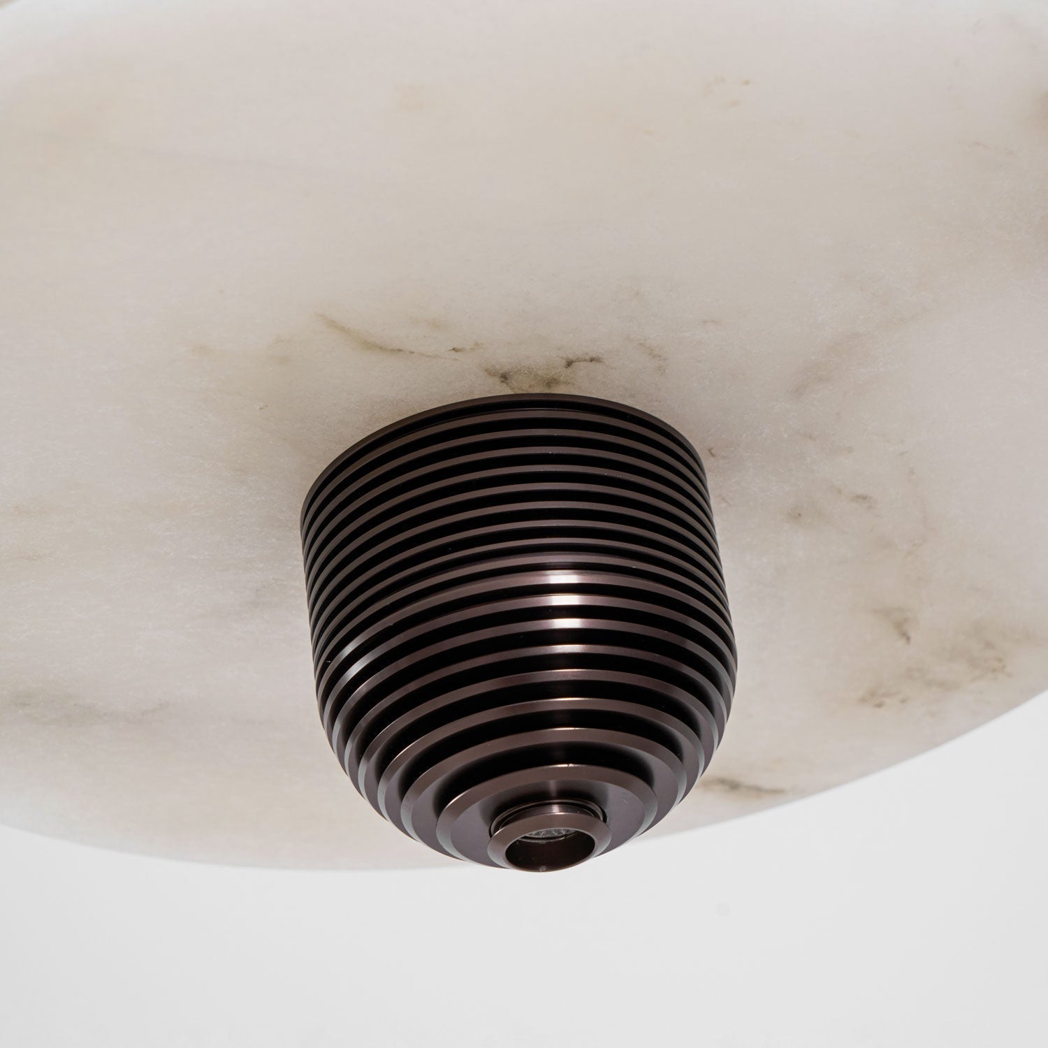 Macro of the ribbed bronze finial under the alabaster disc, showing the stone's grey veining