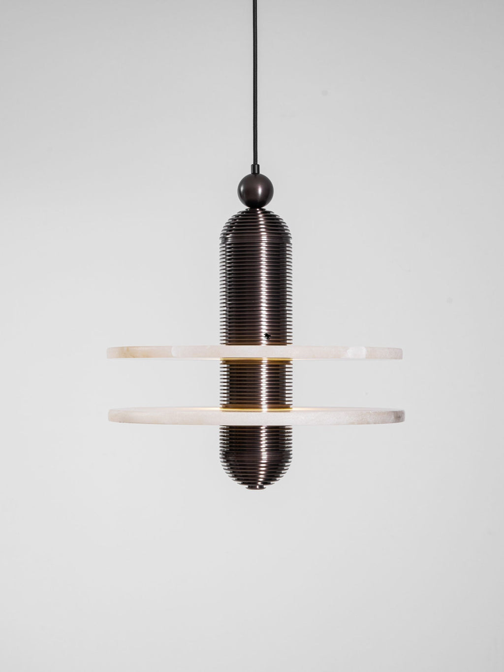 Dark bronze Saturn pendant photographed lit in the studio, a warm band of light between the discs