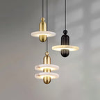 Gold and black Orion pendants grouped at different drops against a soft grey wall, all lit.