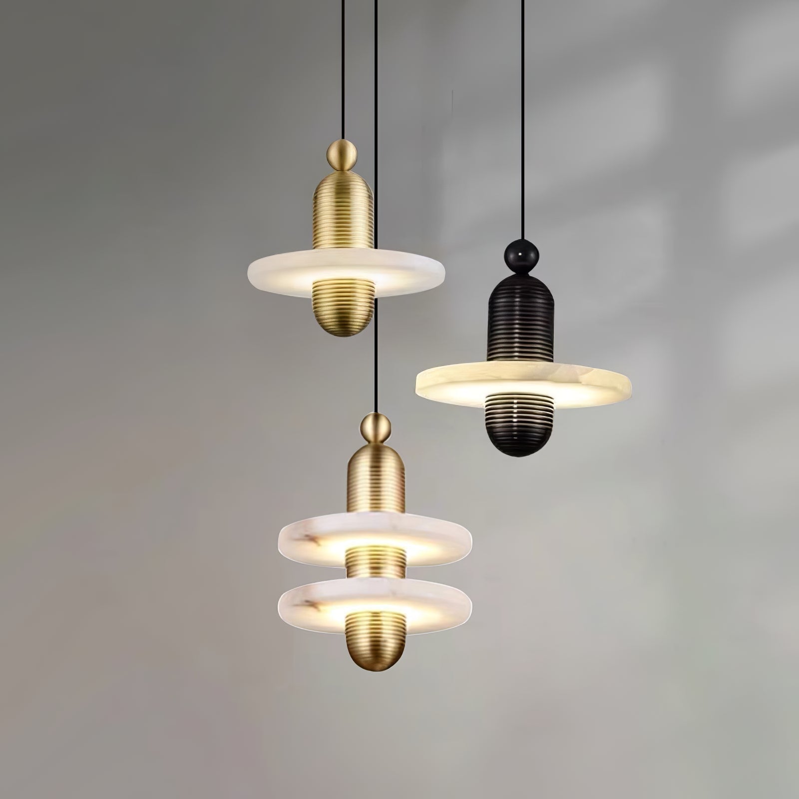 Gold and black Orion pendants grouped at different drops against a soft grey wall, all lit.