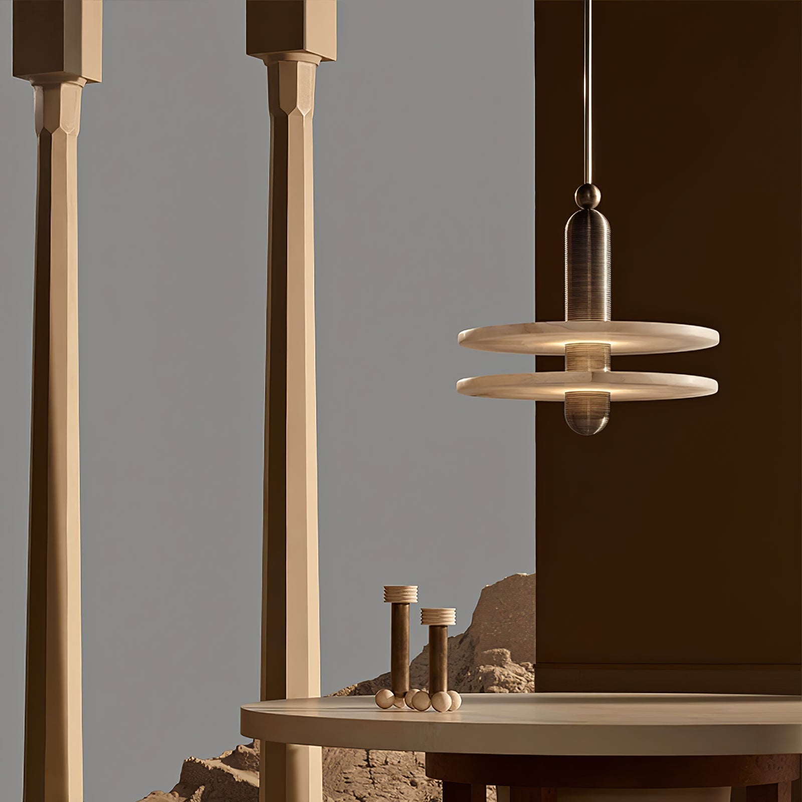 Gold Saturn pendant hanging beside stone columns above a round table in a warm sculptural room