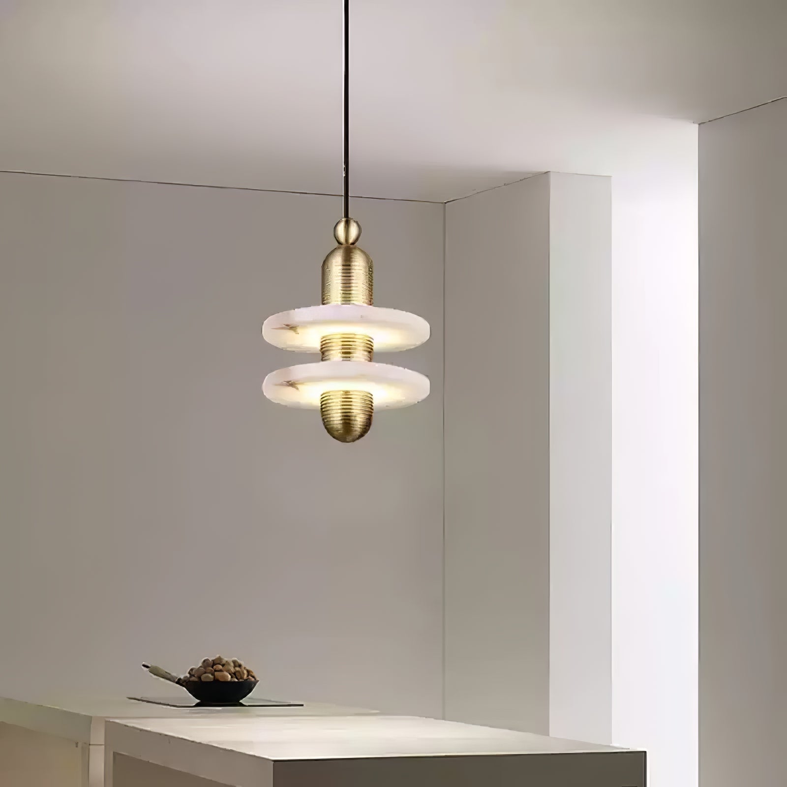 Gold two-disc Orion pendant lit above a white kitchen island in a bright corner.