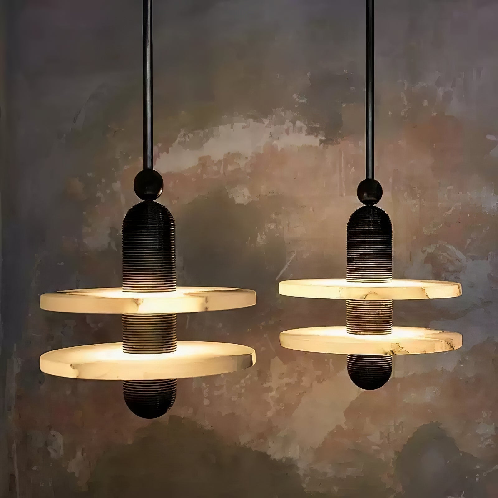 Two black two-disc Orion pendants glowing warm against a weathered plaster wall.