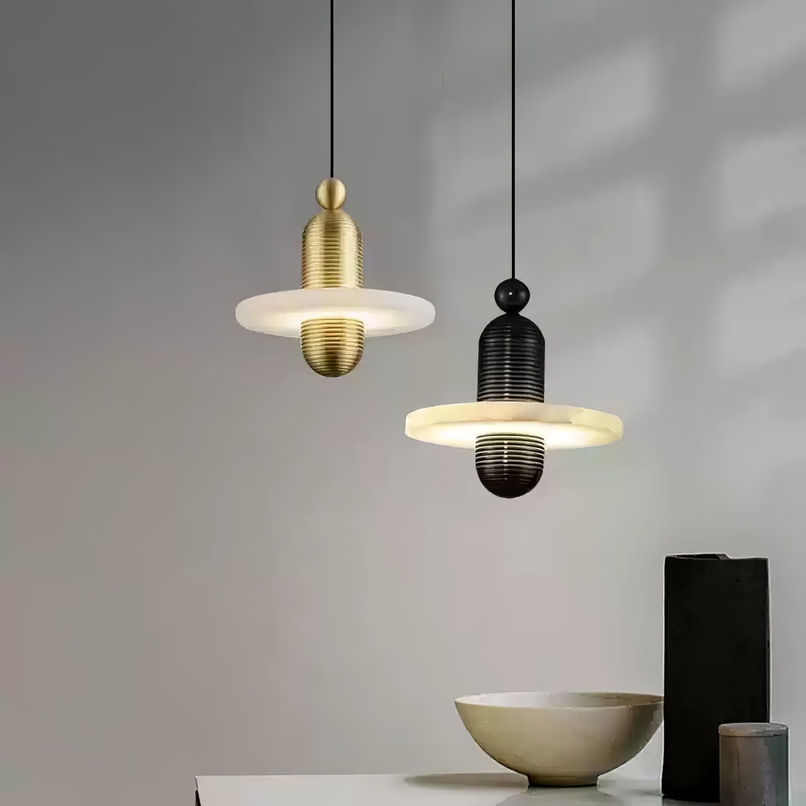 Gold and black single-disc Orion pendants hung side by side above a console with a ceramic bowl.
