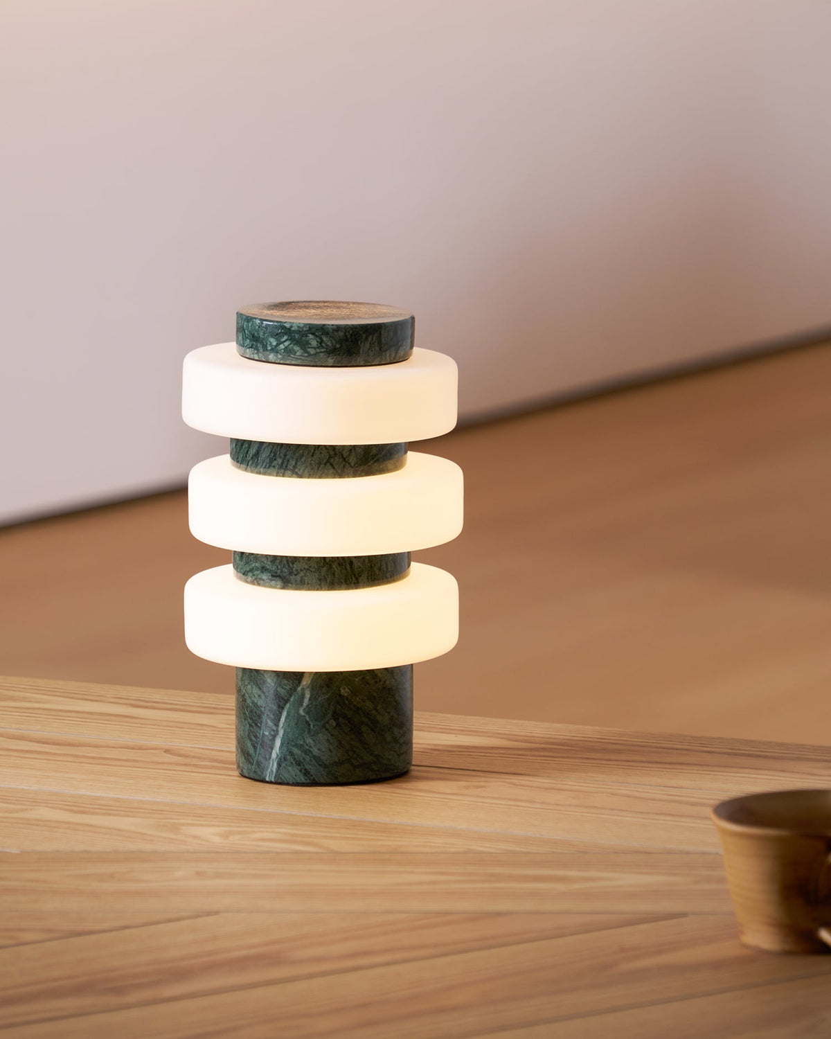 Clérachic green marble table lamp glowing warmly on a wood table, its stone top and base visible beside a bowl.