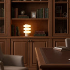 Clérachic travertine table lamp glowing inside a built-in bookcase, framed by leather-bound books and a desk below.