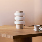 Close crop of the unlit Clérachic stone table lamp on a wood table corner, showing its pale ringed glass shade.