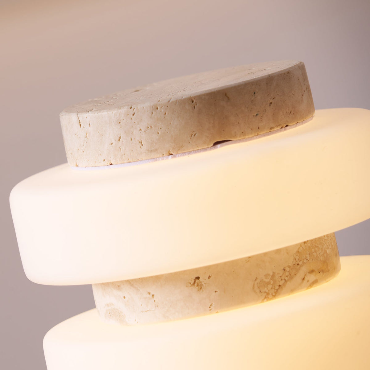 Macro close-up of the Clérachic stone table lamp, showing the travertine top disc resting on a glowing glass ring.