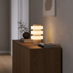Clérachic travertine table lamp glowing on a wood console in a hallway, beside a small plant and stacked books.