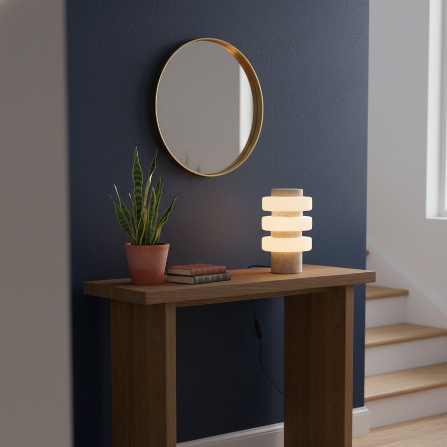 Against a navy wall beside a potted snake plant, a Clérachic travertine table lamp glows on its wood console table.