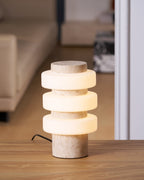 Soft light glows from this Clérachic travertine table lamp near a sofa, seen through a dim living room doorway.
