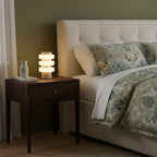 A made bed with floral-patterned pillows sits beside this Clérachic travertine table lamp on the bedside table.