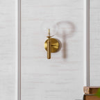 Close to a stack of books, this brass Clérachic wall light's dimpled clear glass globe glows on a panelled wall.