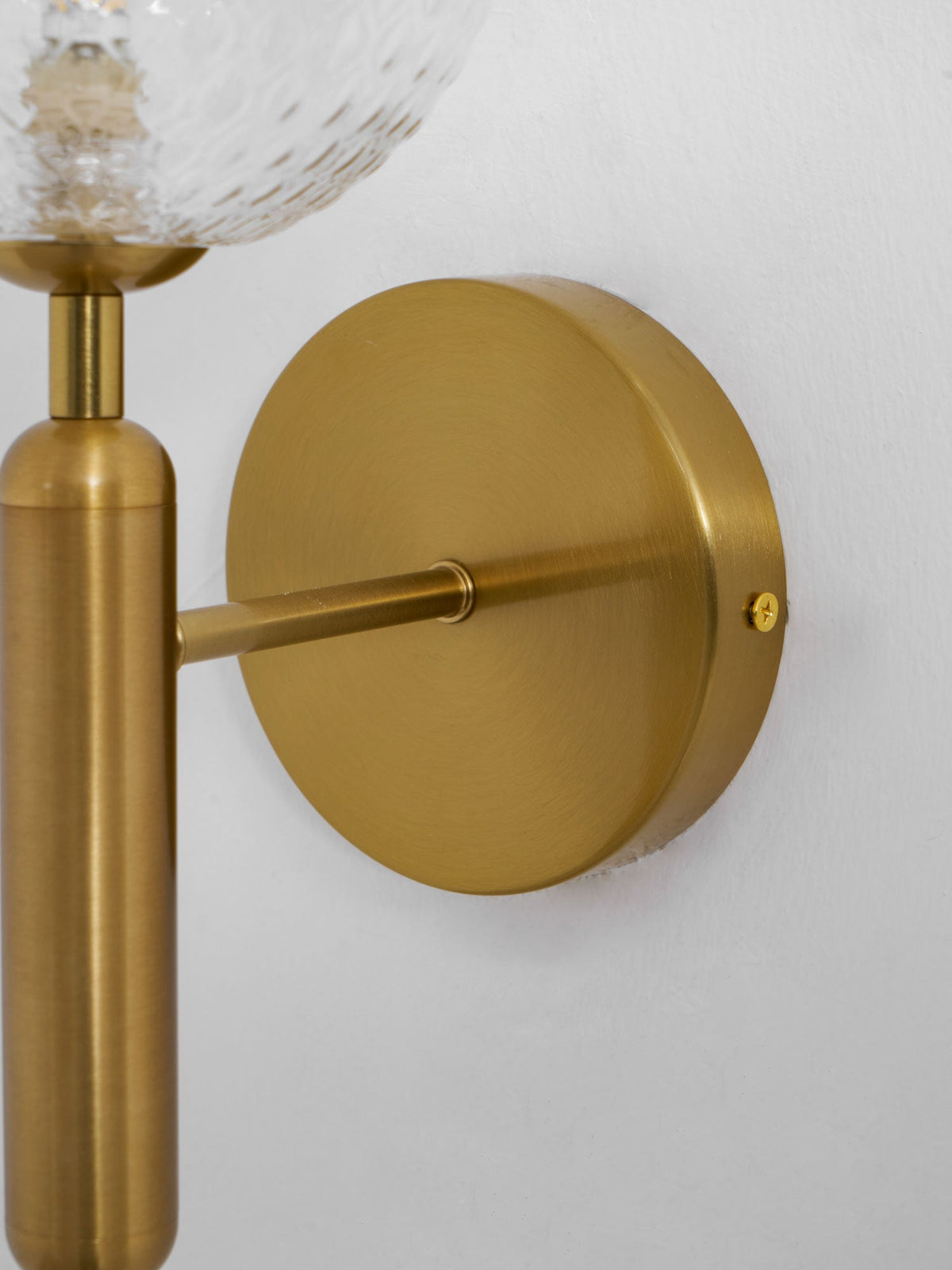 Close view of the brushed brass mounting plate and arm on this Clérachic wall light, its clear glass globe just visible above.