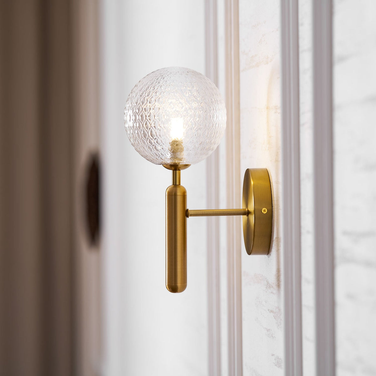 Near a dark doorway with a marble surround, this brass Clérachic wall light's dimpled clear glass globe glows in a hallway.