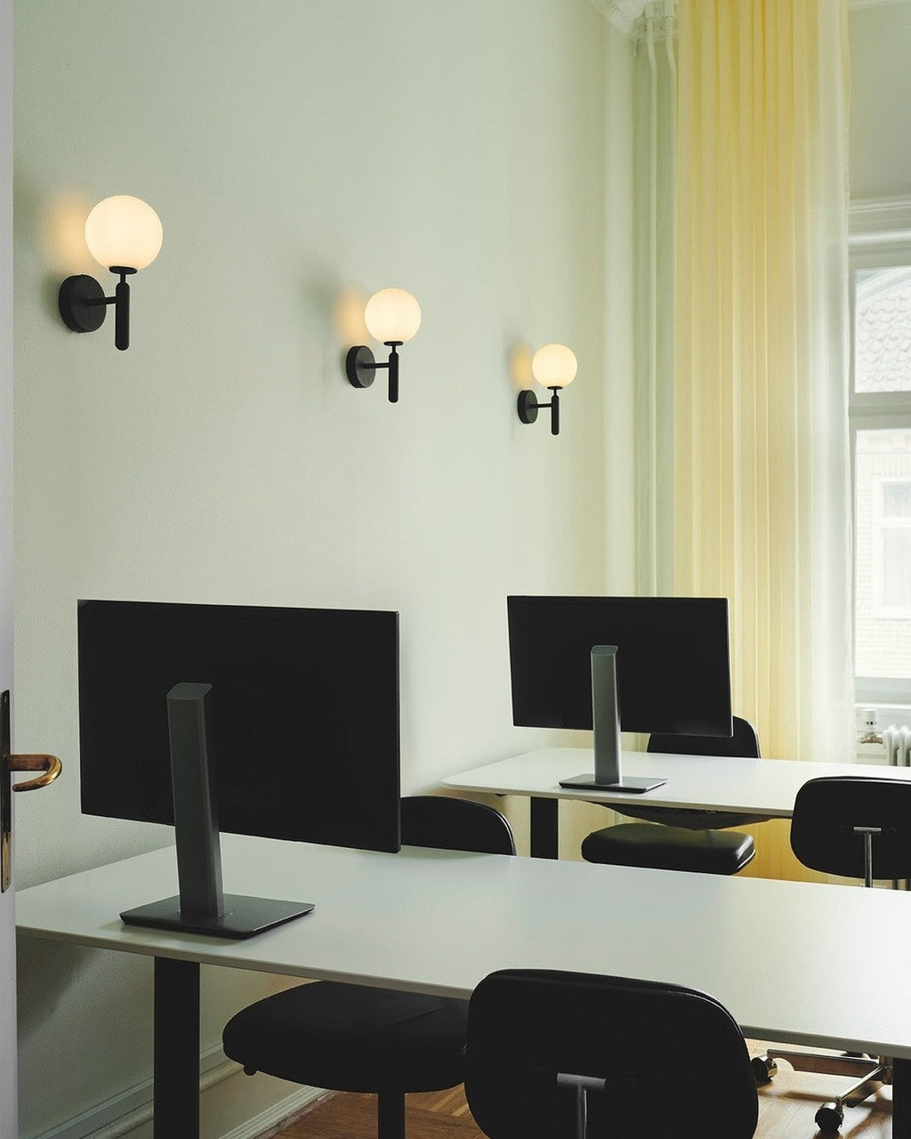 In a mint-green office, three black Clérachic wall lights glow above standing desks with monitors.